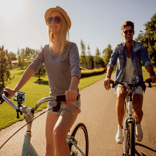 Two friends riding bicycles outdoors enjoying a sunny day, featuring a 4K waterproof action camera mounted on the bike.